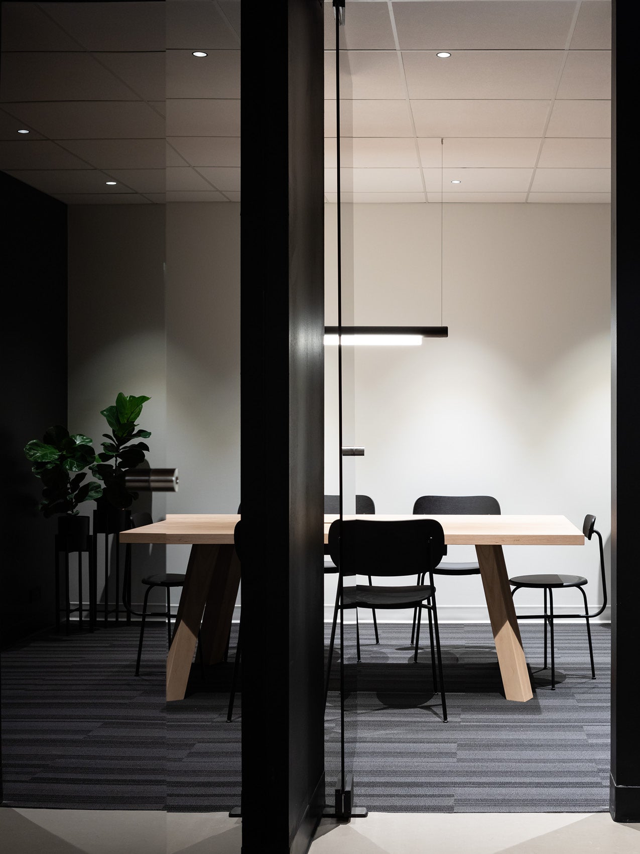 Minimalist meeting room with a light wood table, black chairs and linear black pendant lamp over striped grey carpet