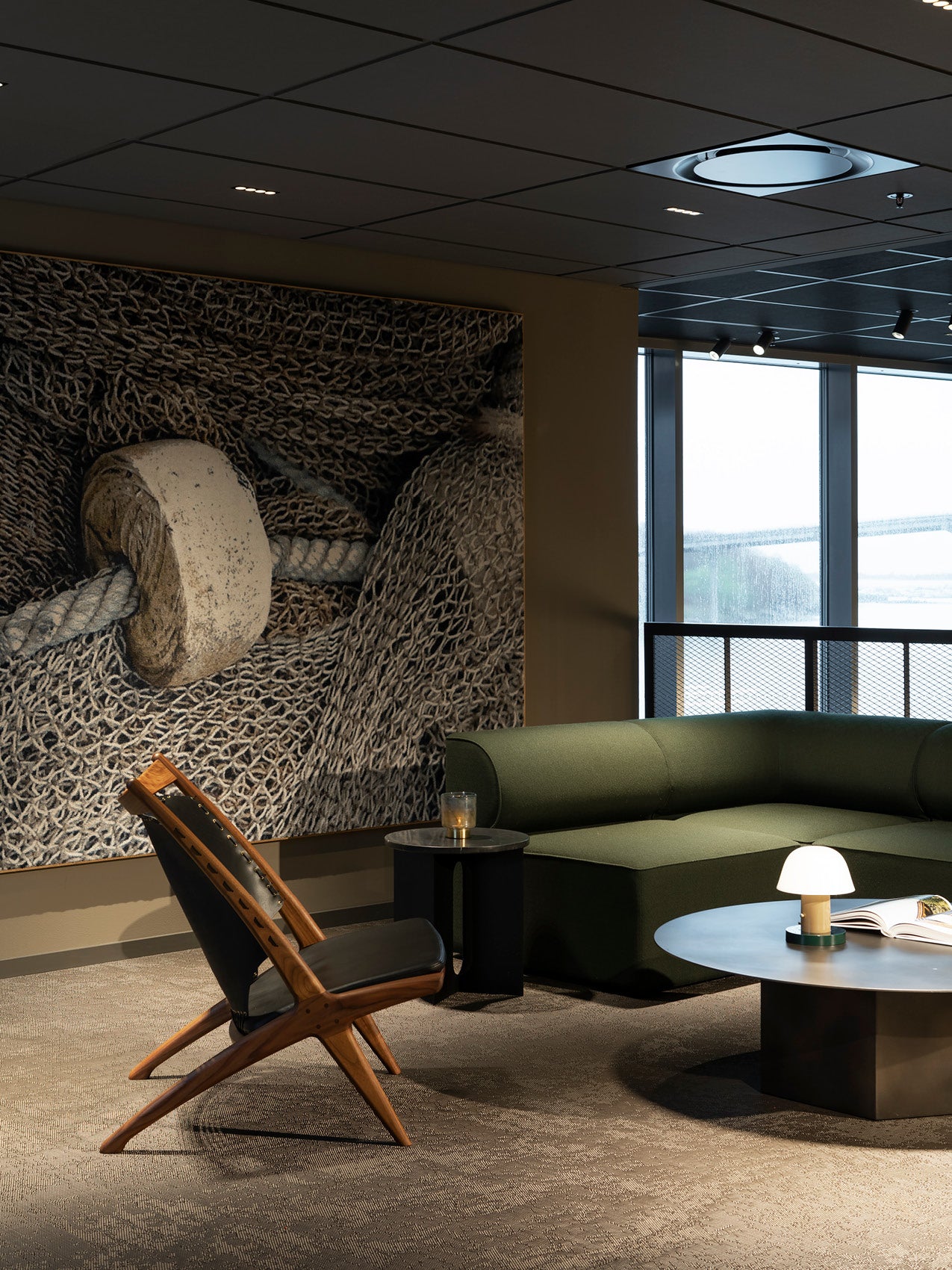 Modern lounge with dark green modular sofa, wooden lounge chair, round black coffee table and textured nautical wall art.