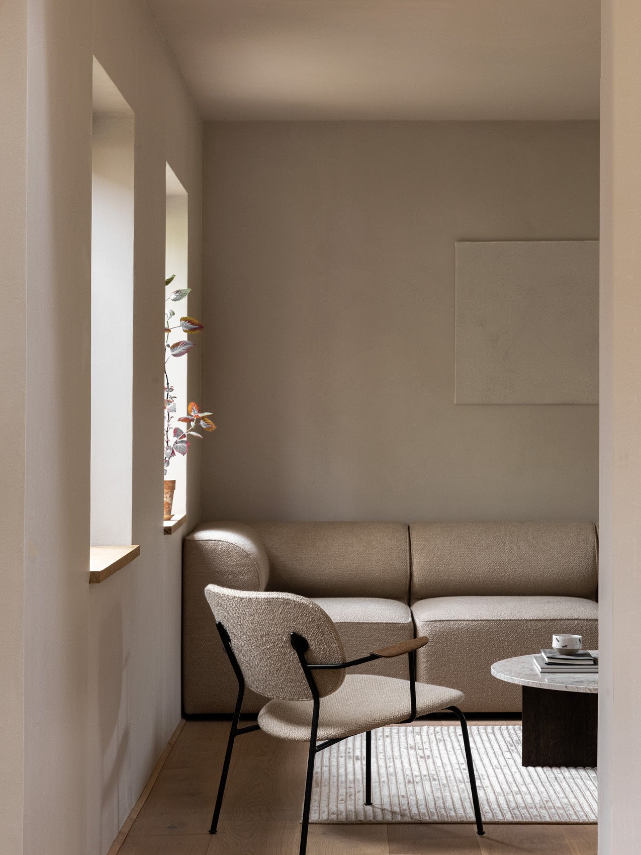 Minimal living room with a beige boucle sofa, matching armchair with black metal frame, marble side table and window plant.