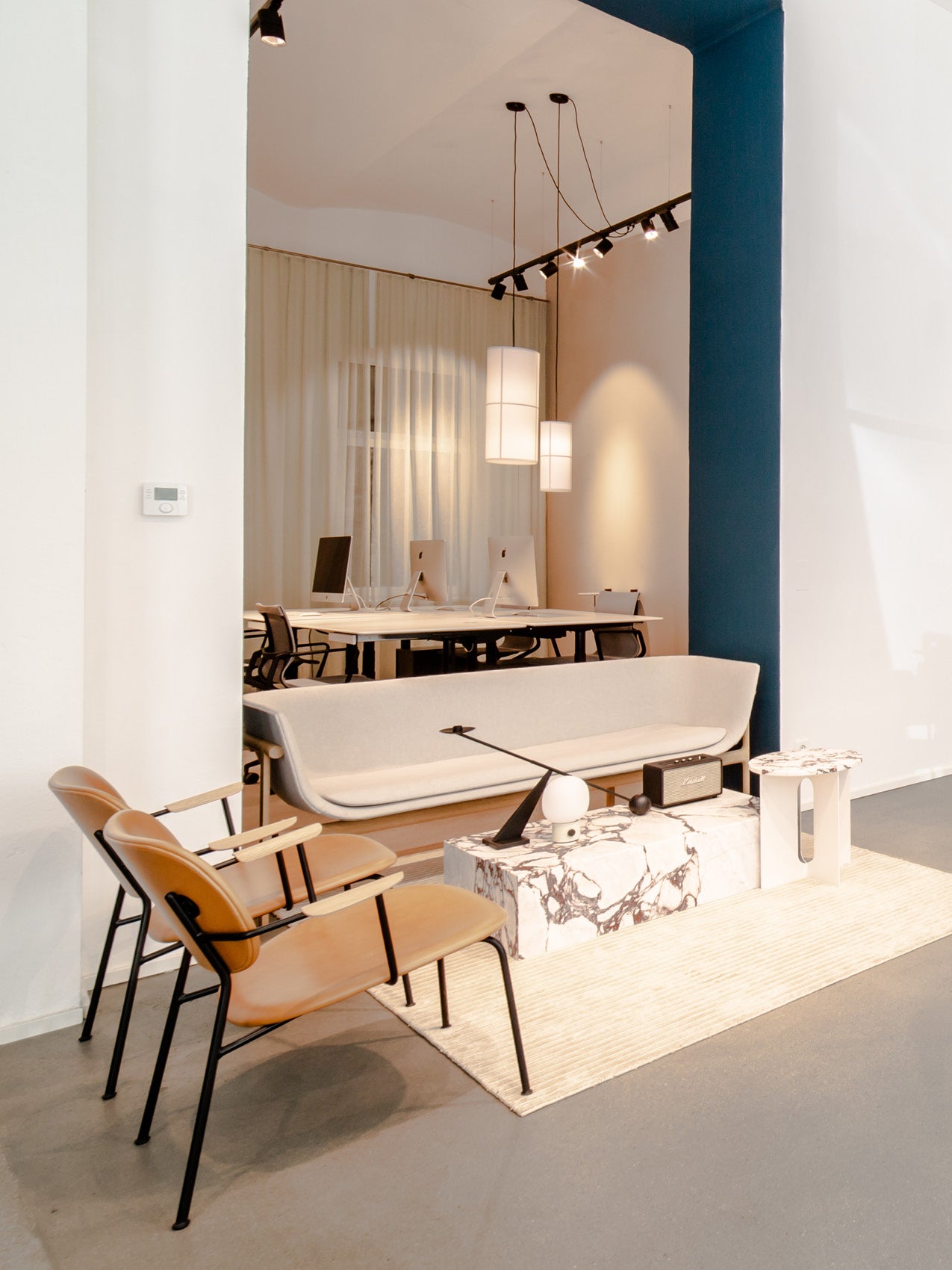 Minimal Danish lounge with beige curved sofa, tan leather chairs, marble coffee table and pendant lights over workspace