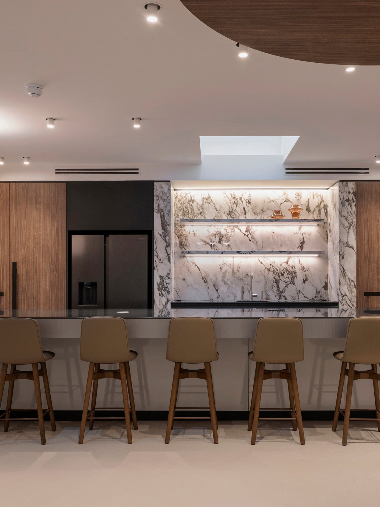 Modern kitchen island with beige leather bar stools, black countertop, marble backsplash and recessed ceiling lights