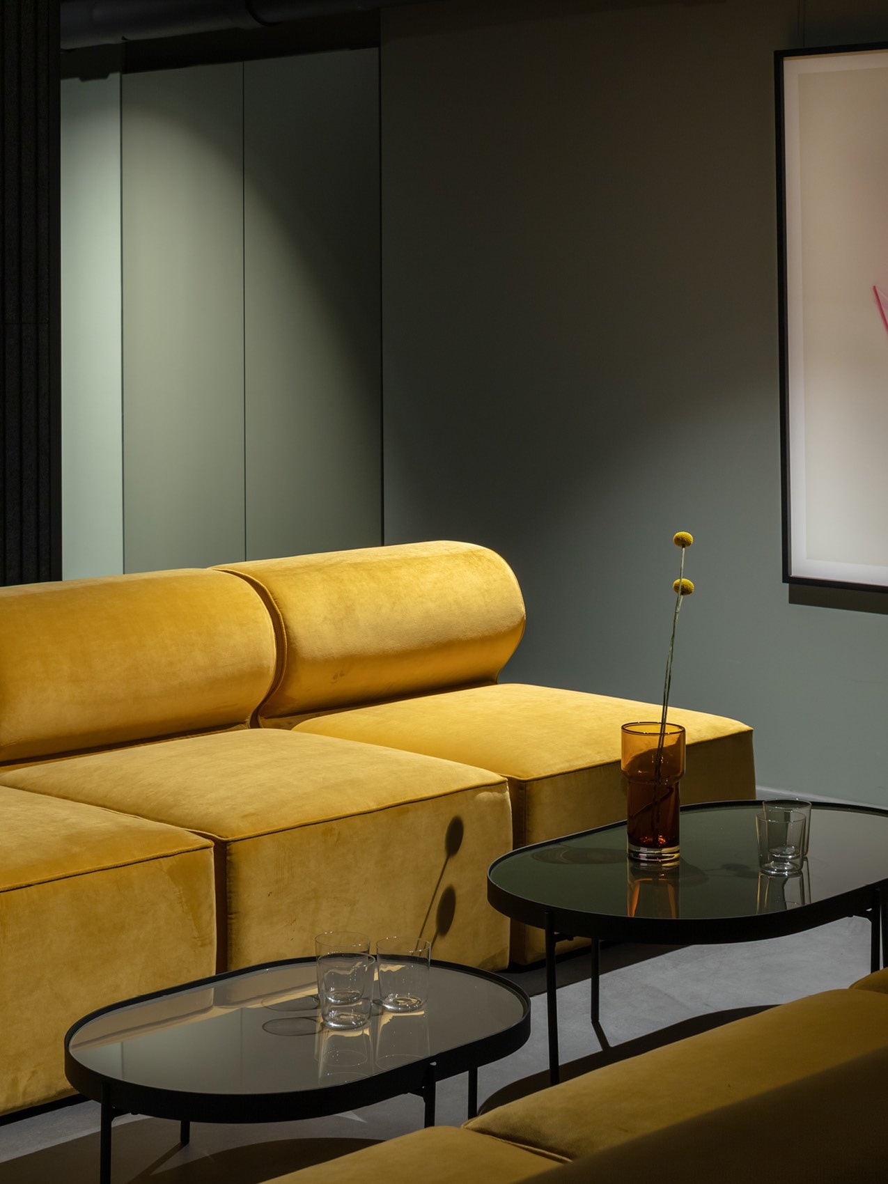 Mustard yellow velvet modular sofa with rounded cushions, black glass coffee tables and amber vase with two billy balls.