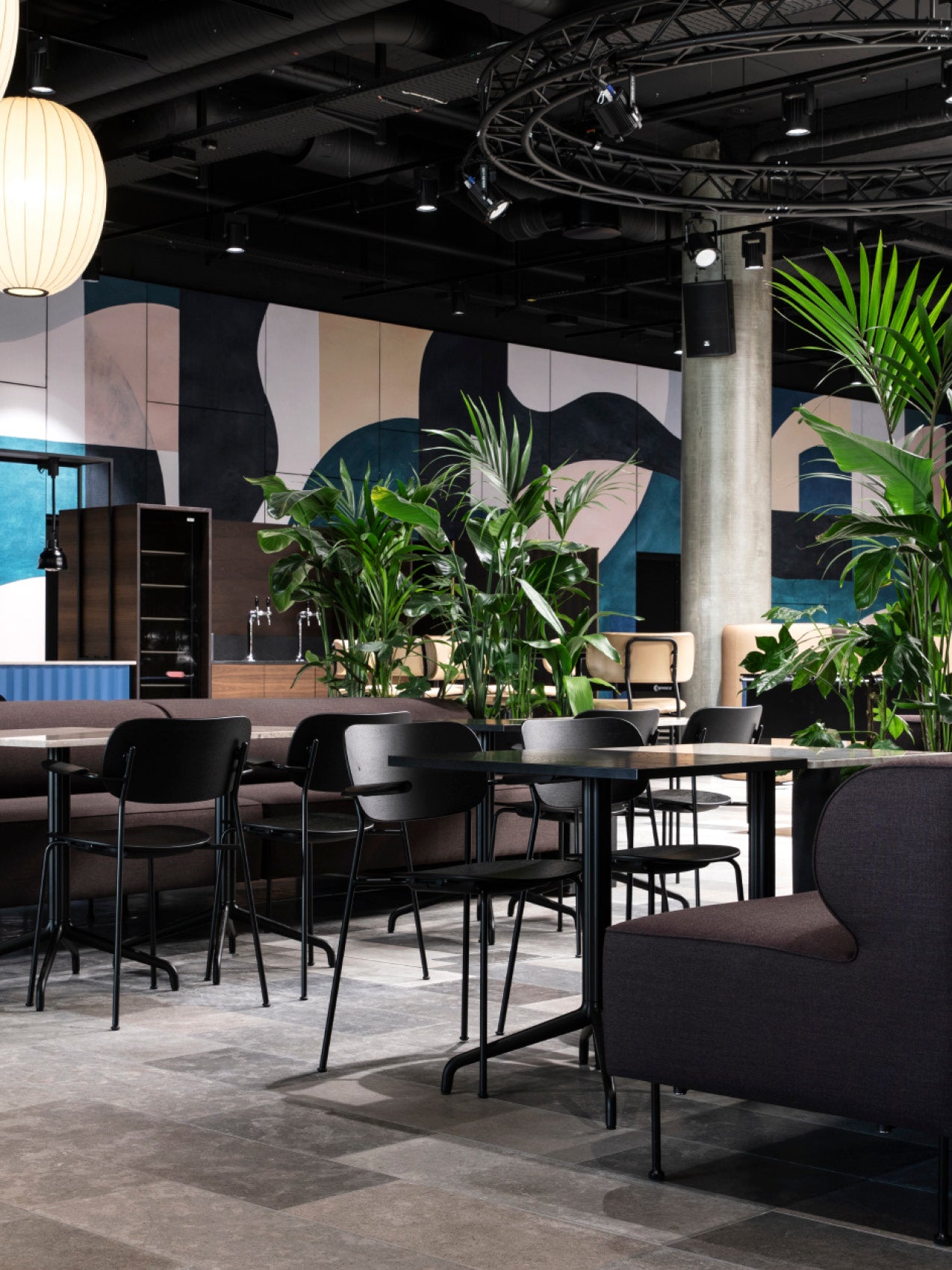 Modern lounge with black metal chairs, dark sofas, round tables and lush green potted plants against abstract wall art