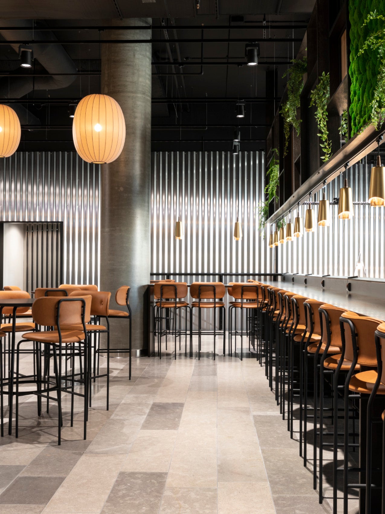 Modern café interior with tan leather high stools, black metal frames, long grey countertop, pendant lights and vertical