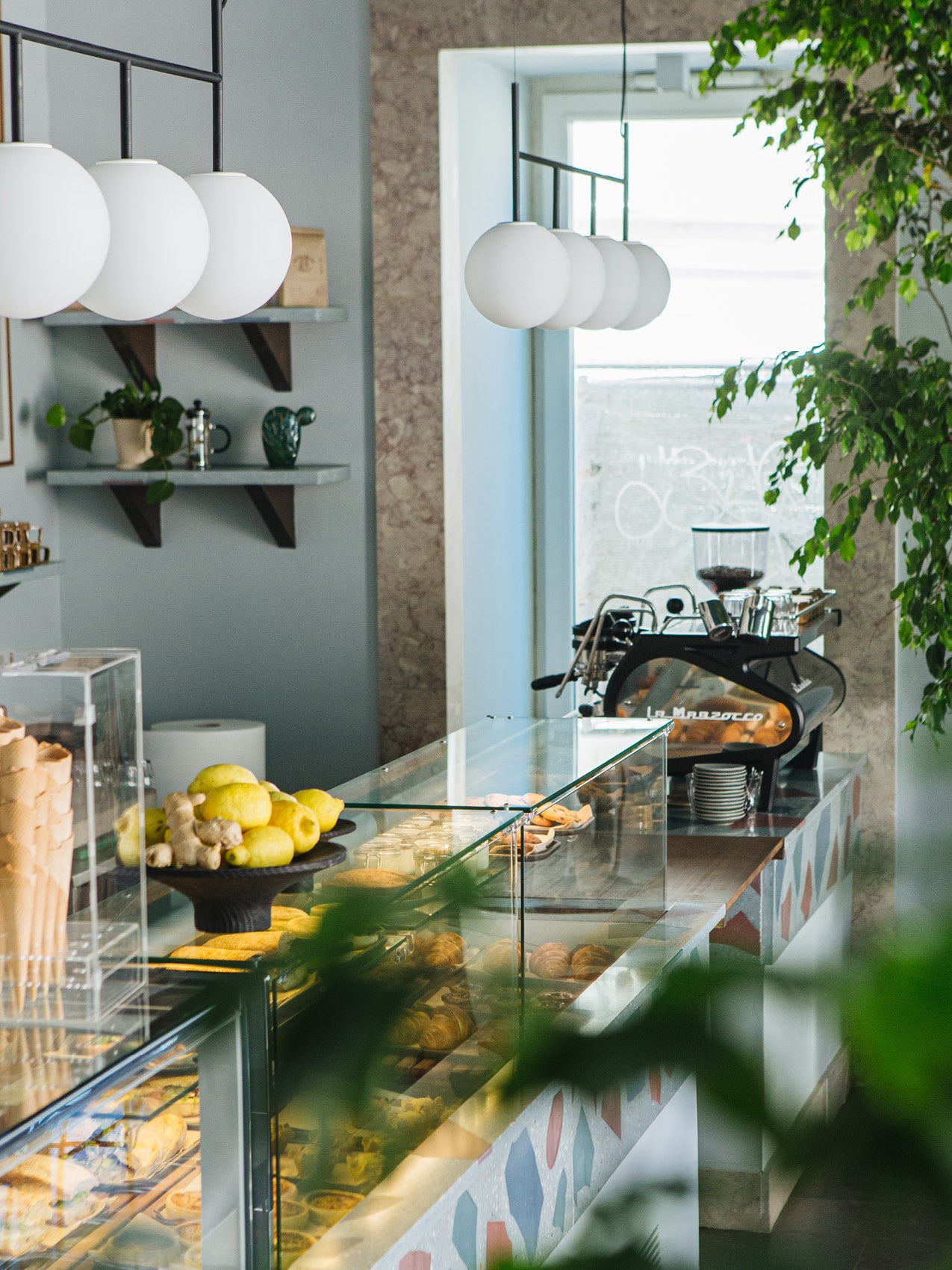Glass bakery counter with pastries, lemons and ginger, matte white globe pendant lights and espresso machine