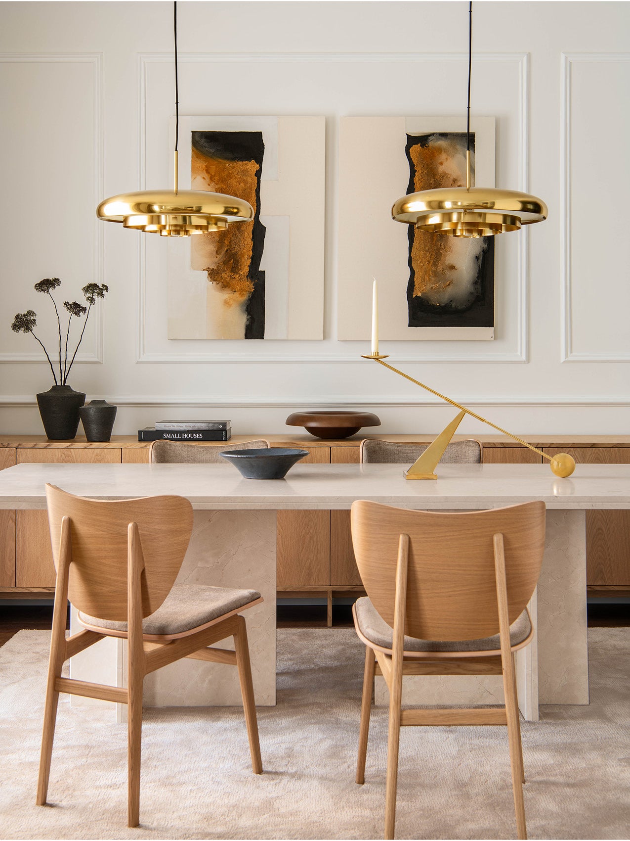 Dining room with two polished brass UFO-shaped pendant lamps, light oak chairs, marble table and abstract wall art