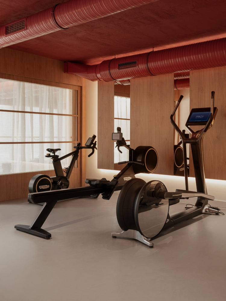 Minimal gym interior with black rowing machine, exercise bike and elliptical, wood panels and red exposed ductwork above