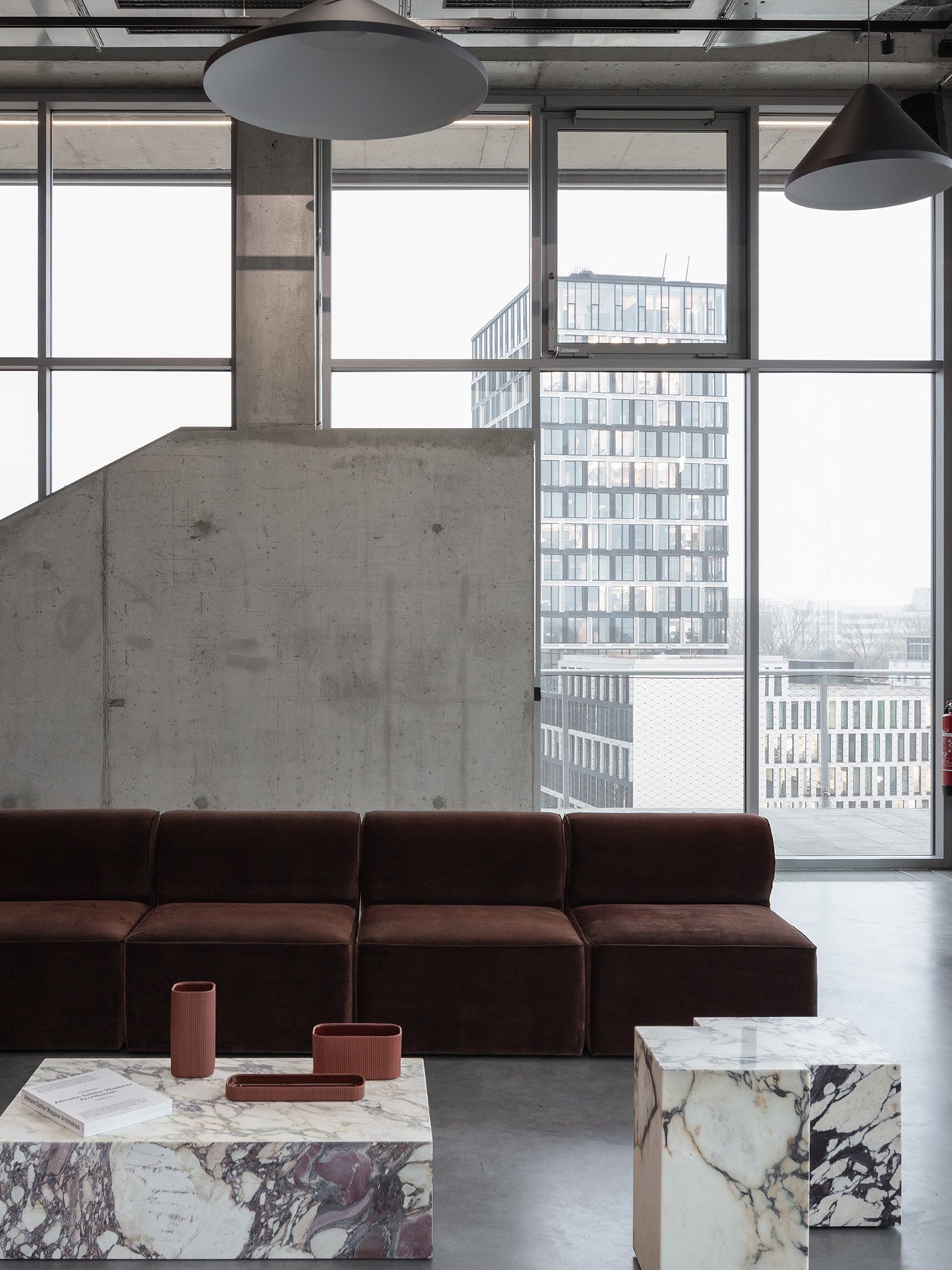 Modern living room with dark brown modular sofa, marble block coffee tables and large windows showing city tower outside