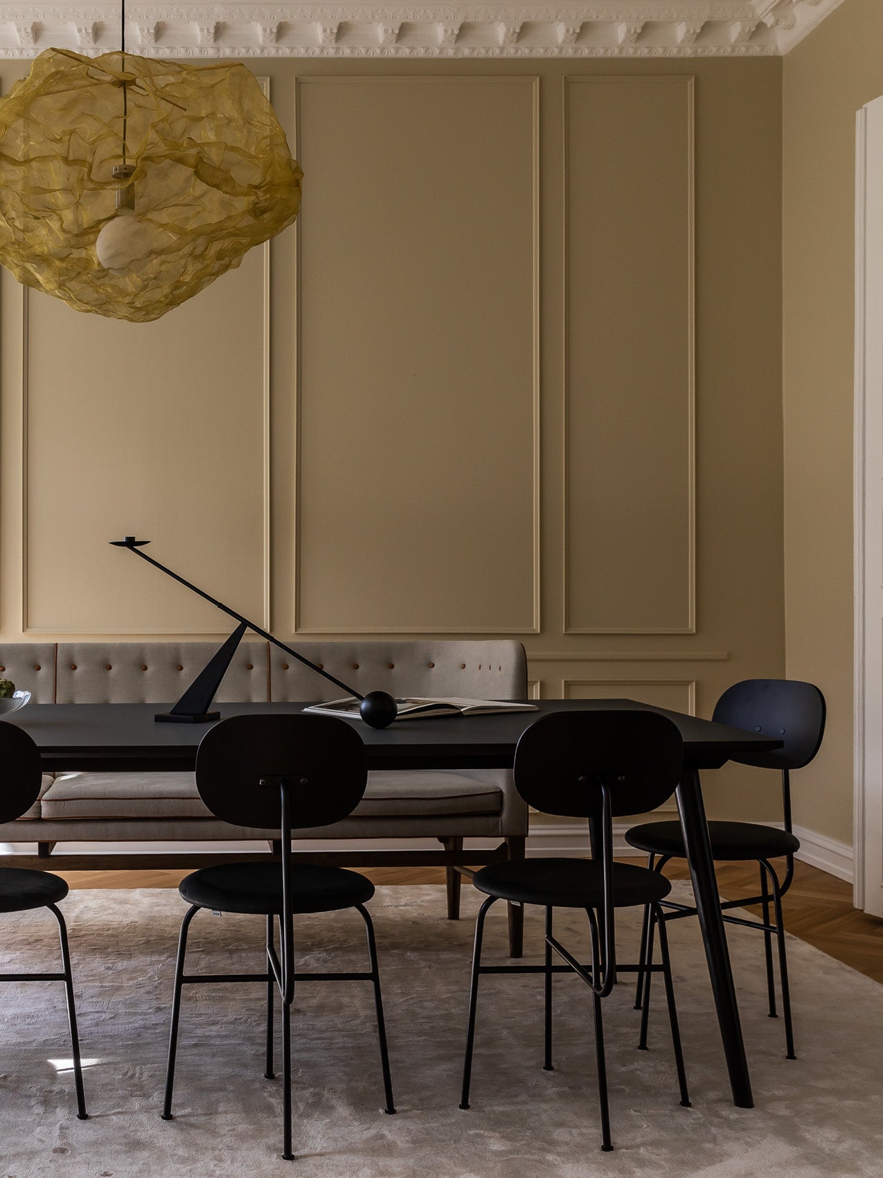 Dining room with black metal table and chairs, beige tufted bench, sculptural yellow organza pendant and minimalist black