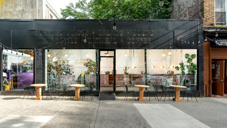 Cafe storefront with black metal facade, large glass windows decorated with white line art, wooden round tables and black