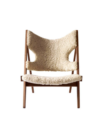 A front view of the Knitting Lounge Chair, featuring a dark walnut wood frame and upholstered in fluffy, natural sheepskin.