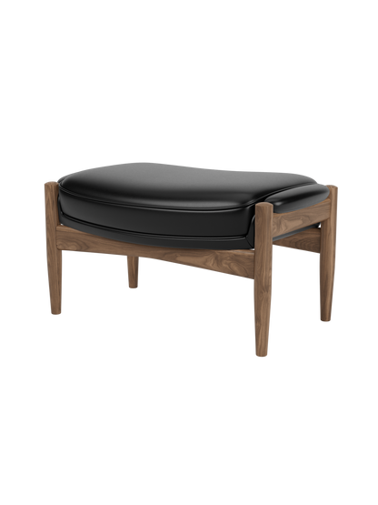 A three-quarter view of The Seal Ottoman, featuring a solid walnut frame with curved supports and a padded black leather top.