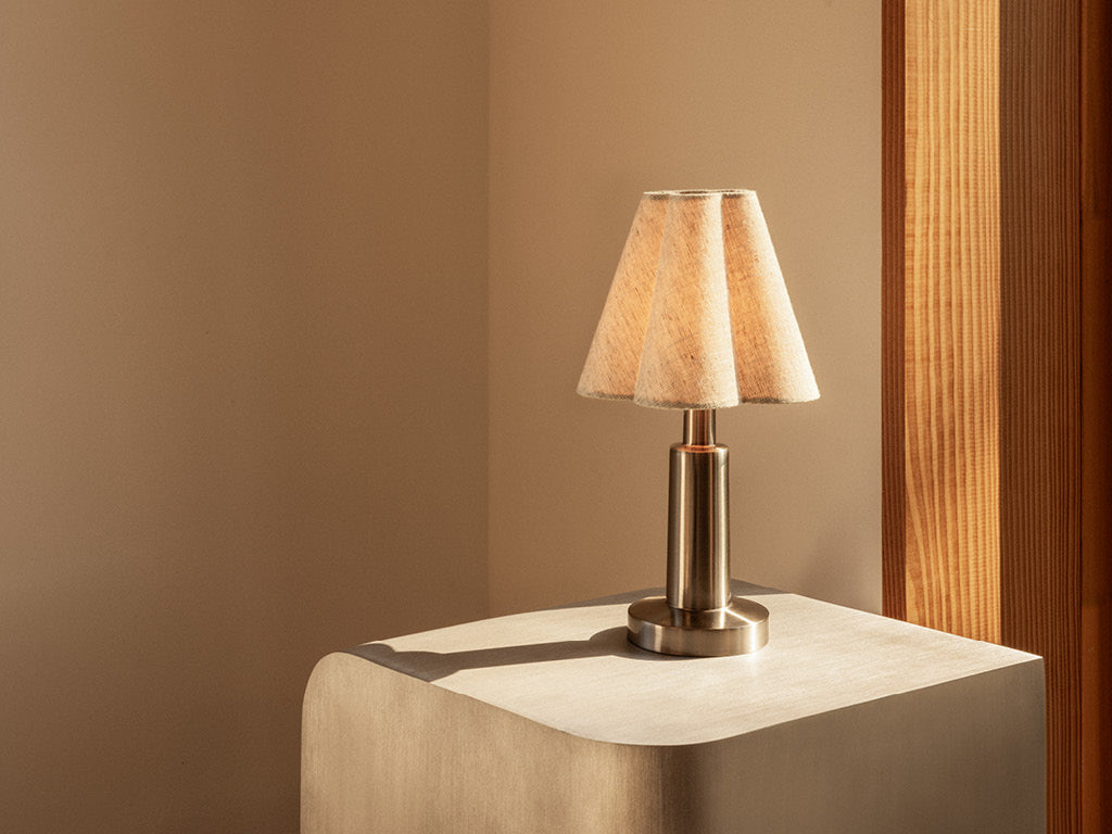 Small brass table lamp with a beige fabric shade casting a shadow on a light wood side table