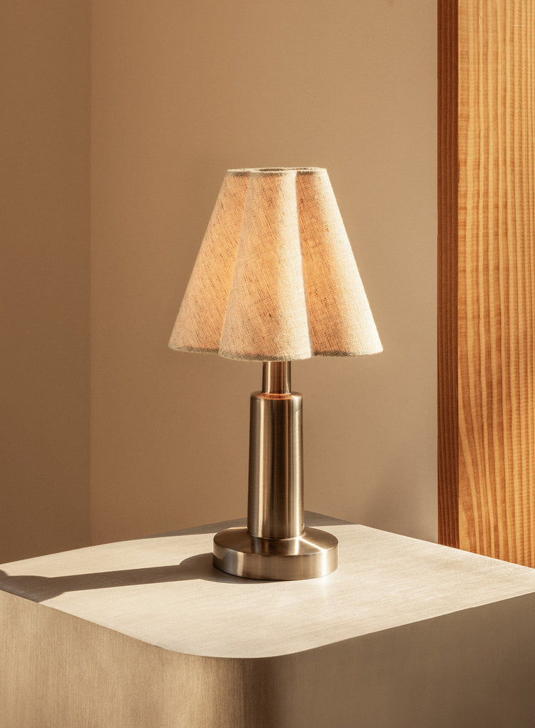 Small table lamp with a pleated beige fabric shade and brushed metal base on a light wooden pedestal