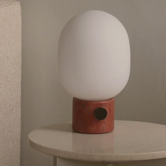 White rounded frosted glass lamp on a cylindrical terracotta base with black circular switch on a cream marble table