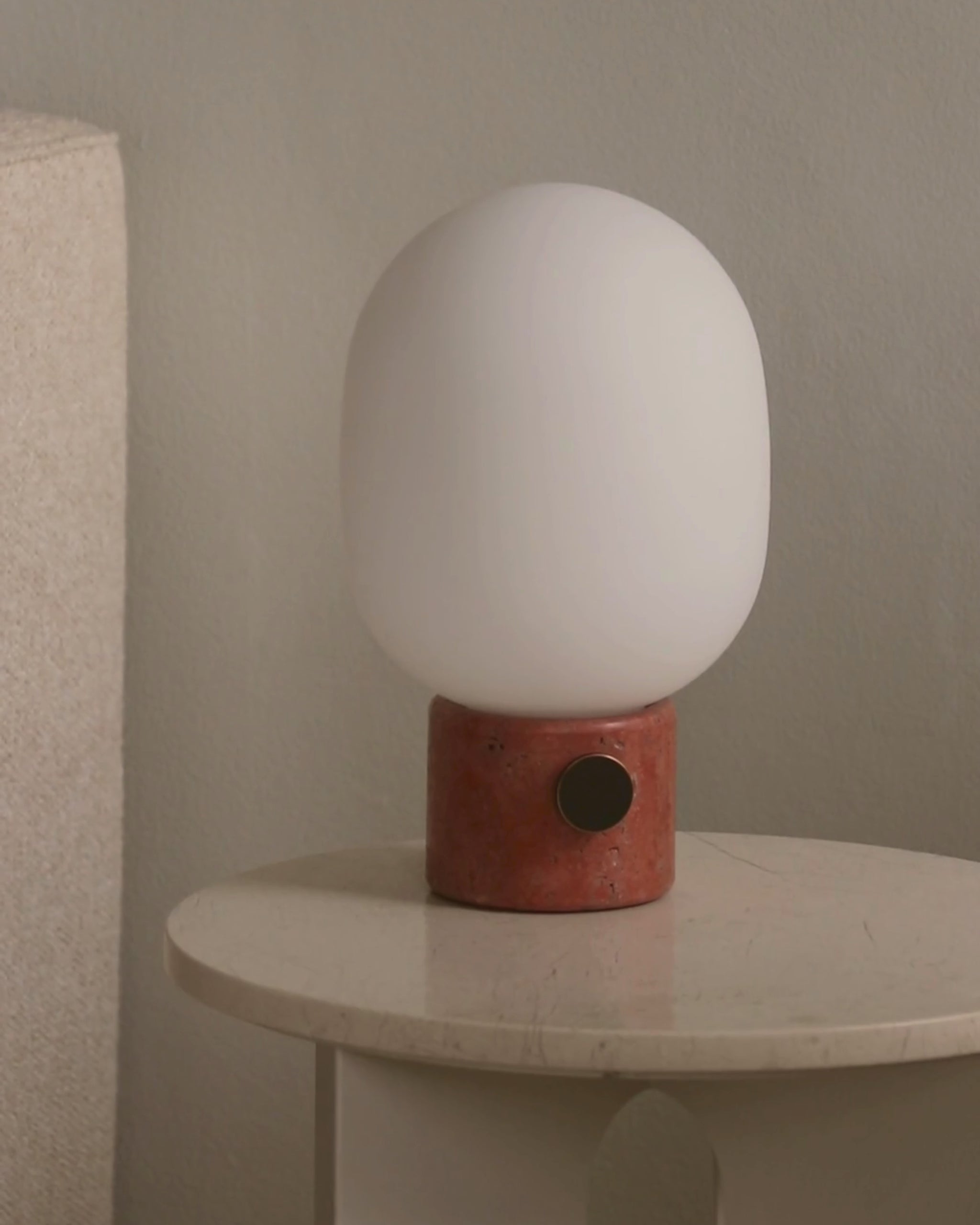White rounded frosted glass lamp on a cylindrical terracotta base with black circular switch on a cream marble table