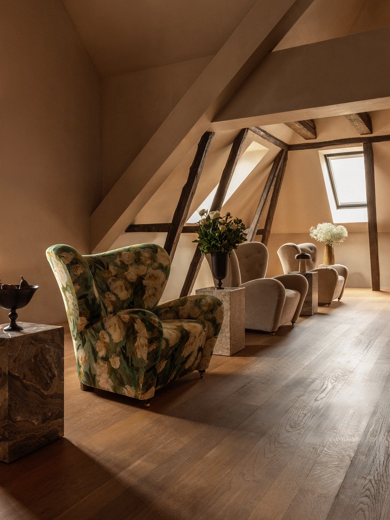 Attic seating area with floral green velvet wingback armchair, beige upholstered lounge chairs, wooden beams and marble side