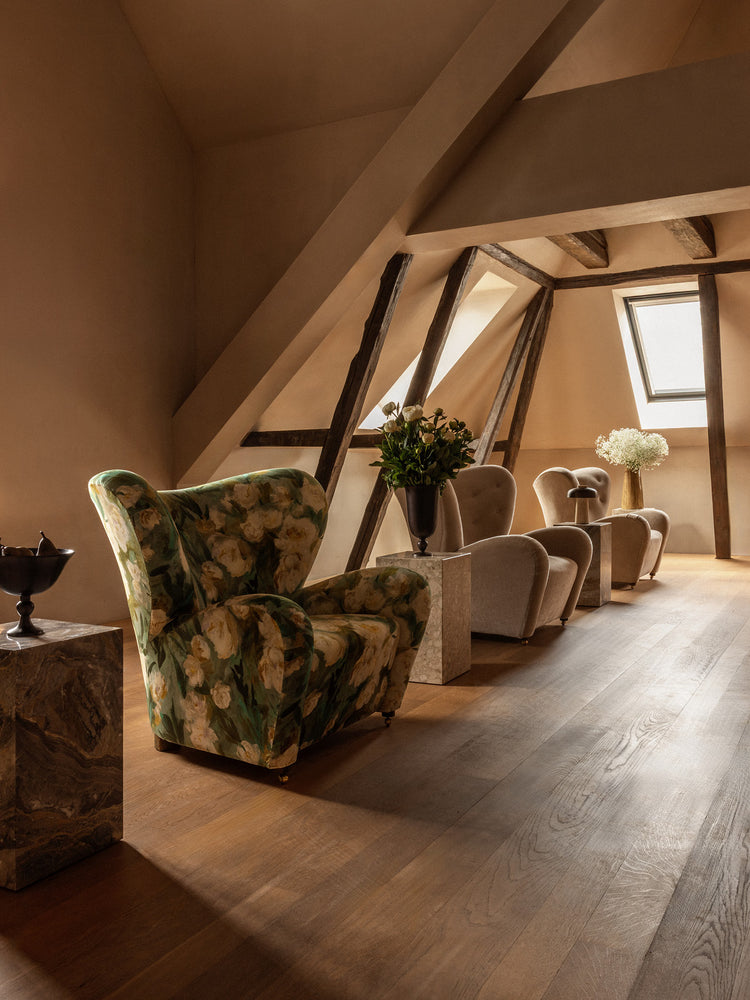 Attic seating area with floral green velvet wingback armchair, beige upholstered lounge chairs, wooden beams and marble side