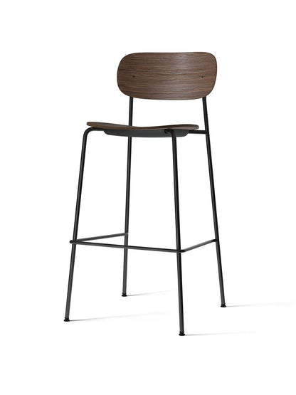 The Co Bar Chair, viewed at an angle, featuring a dark stained oak veneer seat and backrest on a slender, black steel frame.