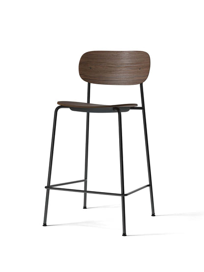 An angled view of the Co Counter Chair, featuring a dark stained oak veneer seat and backrest on a slender black steel frame.