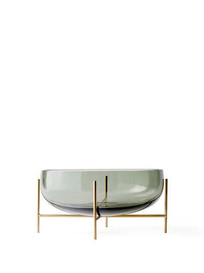 Front view of the Echasse Bowl, a wide, smoked green glass bowl on a slender, minimalist brass-coloured stand.