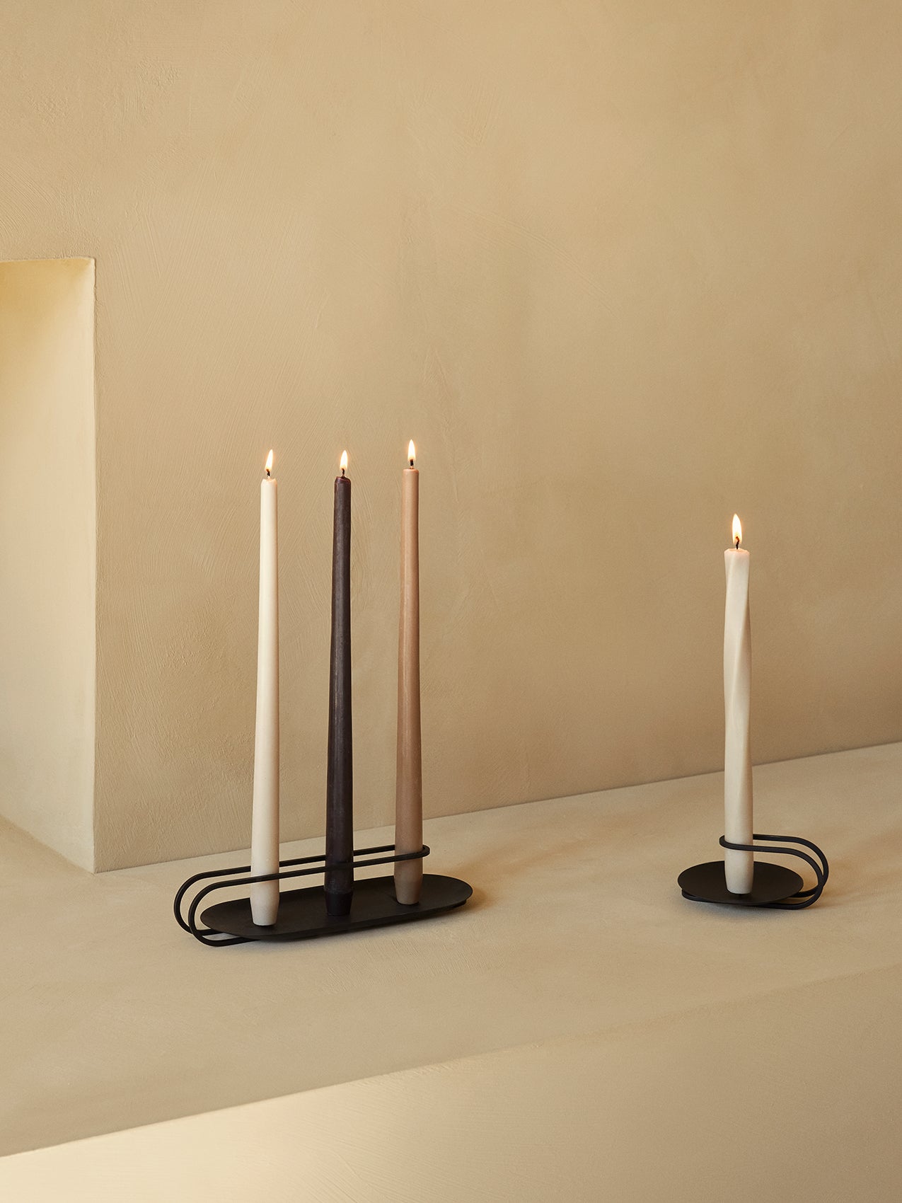 Two black metal Clip Candle Holders. One holds three lit Spire candles, and the other holds one lit Twist candle.
